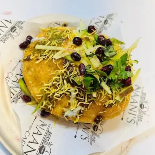 A golden fried flatbread topped with green chutney, sev, pomegranate seeds, and fresh herbs.