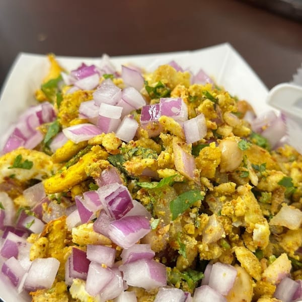 Close-up of a dish with yellow scrambled eggs, green herbs, and diced red onions.