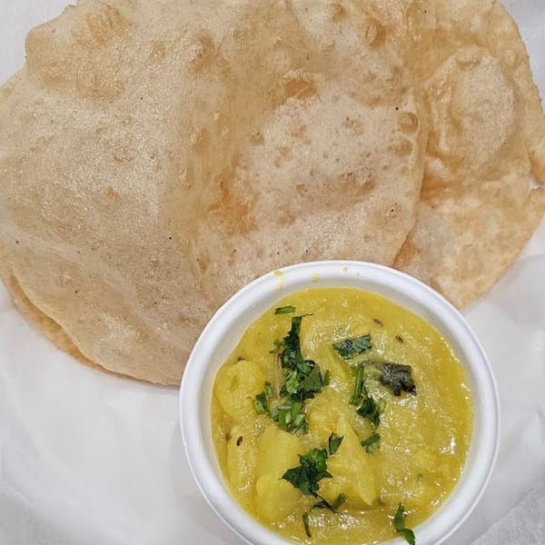 Two golden-brown puri breads served with a small bowl of yellow potato curry garnished with cilantro.