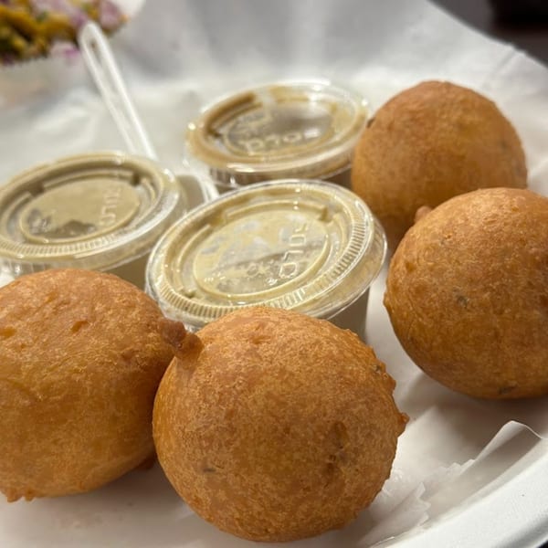 Four golden-brown hushpuppies and three small containers of dipping sauce on a white plate.