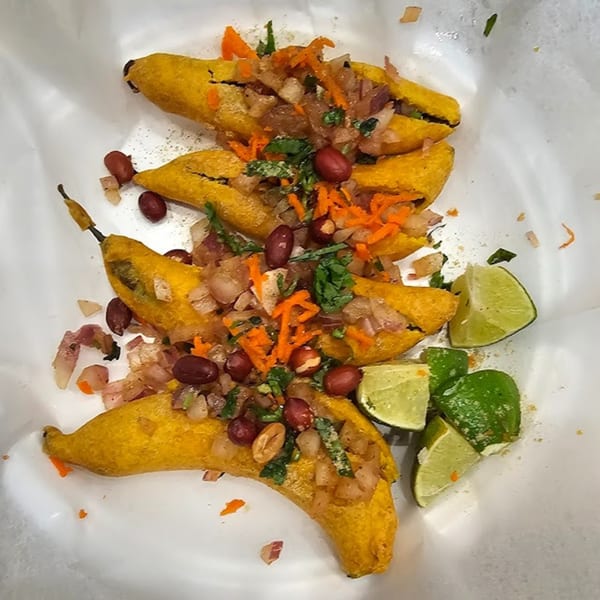 Four fried plantains stuffed with vegetables, peanuts, and cilantro, served with lime wedges.